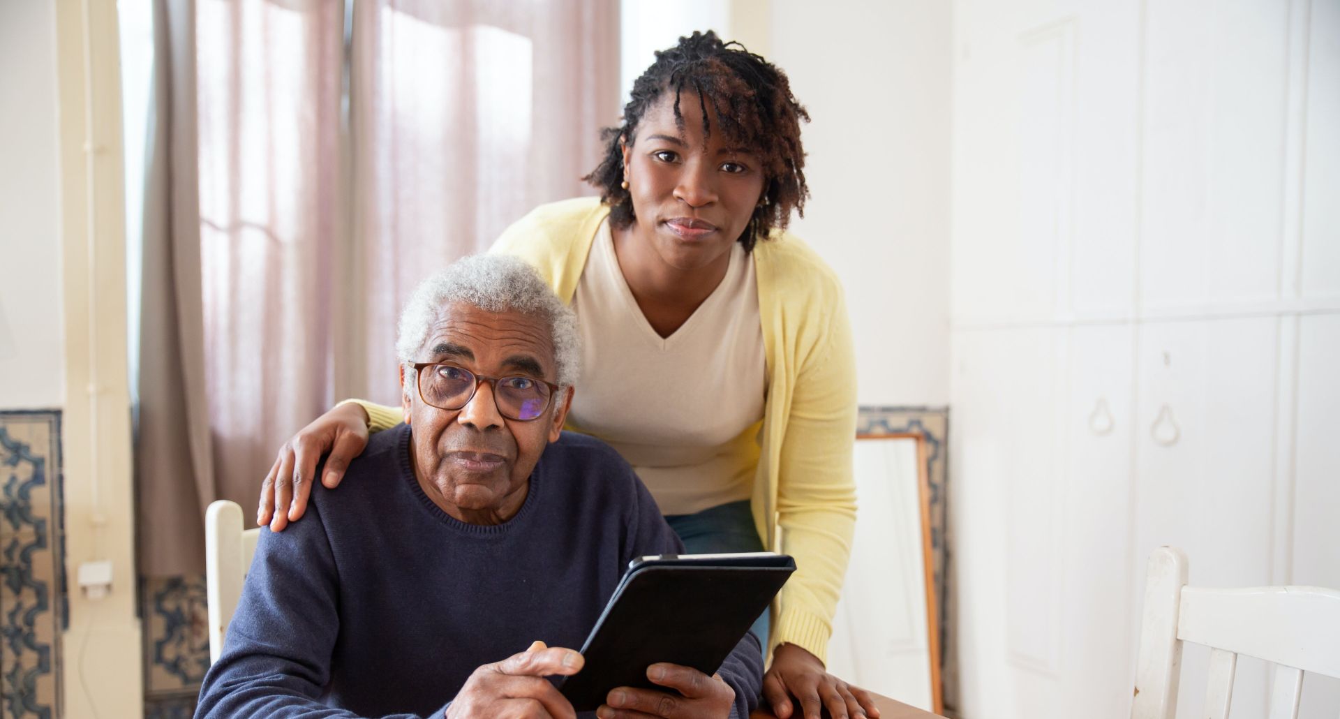 A Woman Standing Beside the Elderly Man Holding a Tablet